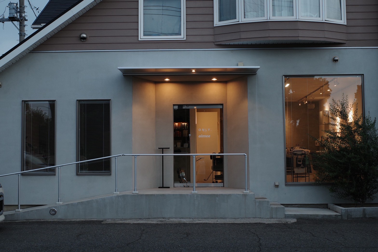 モダンな美容サロンの外観 - 夕暮れ時のライトアップされた高級感あふれるエントランス、ONLY aimeeの看板、洗練された現代建築デザイン