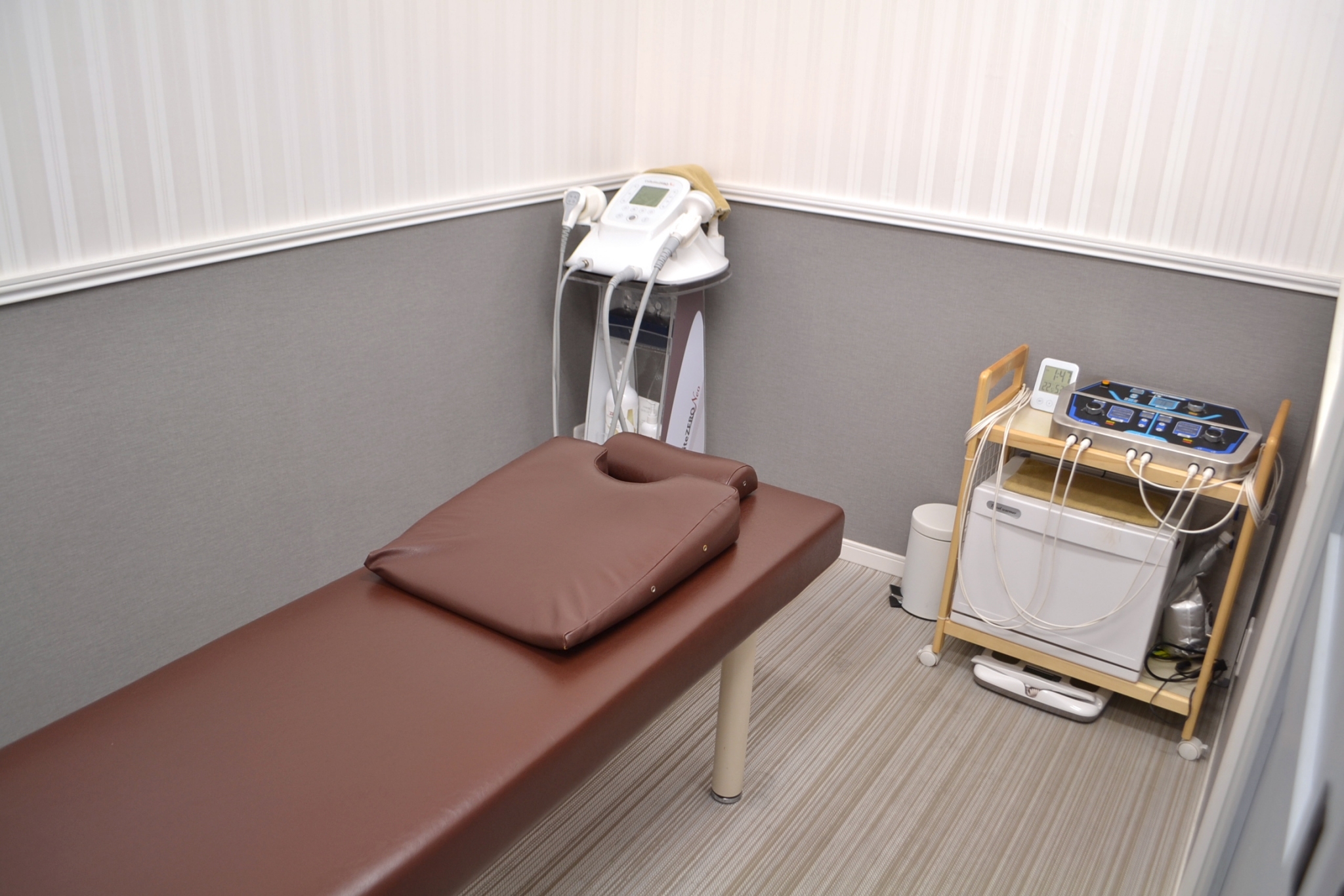 整体サロンオーナーの施術室 - Growth Partners Japan導入事例 整体サロン施術室内観 ブラウンの施術ベッドと専門機器を備えた清潔な治療空間 福岡 30代女性オーナー経営